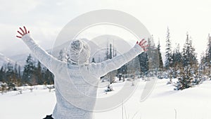 Young woman waching the snowfall and rising her hands on the mountain