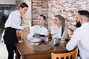 Young woman waiter receiving order from guests