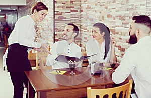 Young woman waiter receiving order from guests