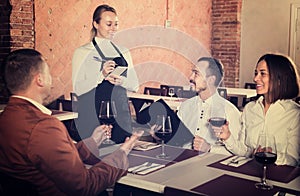 Young woman waiter receiving order from guests in restaurant