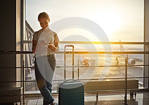 young woman waiting for flying at airport at window with suitcase .