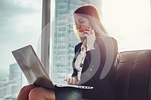 Young woman waiting in a hall sitting in modern office working on laptop talking on the phone