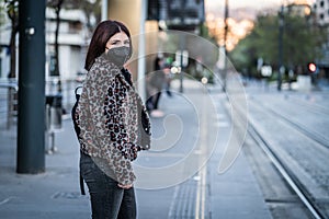 Young woman waiting for the tram with the mask against the coronavirus