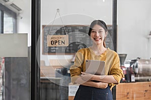 Young woman is a waitress in an apron, the owner of the cafe stands at the door with a sign Open waiting for customers