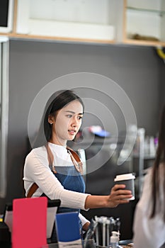 Young woman waitress serving cup of coffee to customer in coffee shop.