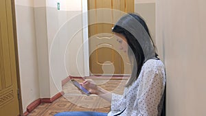 Young woman waits her turn for job interview browsing phone sitting near door.