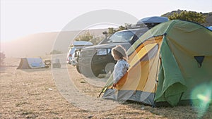 Young woman wakes up and comes out from tourist tent and stretches