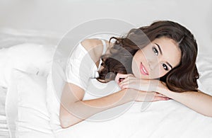 Young woman wakes up in a white bed in the morning