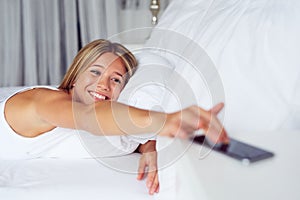 Young woman waking up with mobile alarm clock