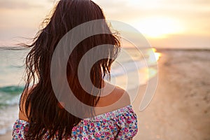 Young woman walk on an empty wild beach towards celestial beams of light falling from the sky,