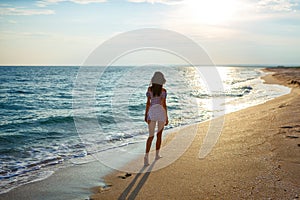 Young woman walk on an empty wild beach towards celestial beams of light falling from the sky,