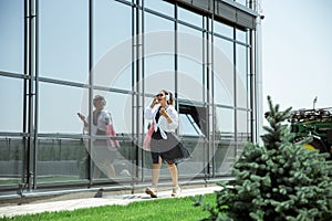 Young woman walking against glass` wall in airport, traveler with small baggage, influencer`s lifestyle