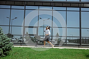 Young woman walking against glass` wall in airport, traveler with small baggage, influencer`s lifestyle
