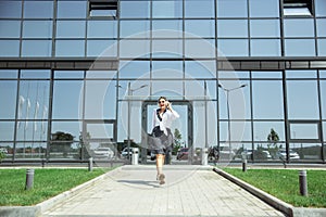 Young woman walking against glass` wall in airport, traveler with small baggage, influencer`s lifestyle