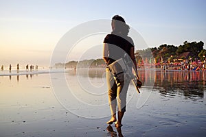 Young woman walking alone on beach at sunset with bare foot. Seminyak Beach, Bali, Indonesia