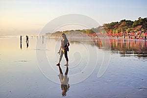 Young woman walking alone on beach at sunset with bare foot. Seminyak Beach, Bali, Indonesia