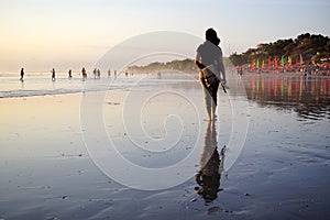 Young woman walking alone on beach at sunset with bare foot. Seminyak Beach, Bali, Indonesia