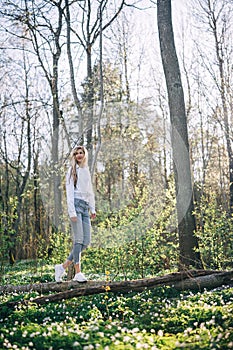 Young woman is walking along a fallen tree in a forest covered with blooming white wood anemones