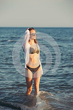 Young woman walking along sea or ocean beach at sunset