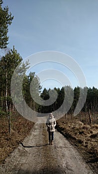 Young woman walking away alone on a forest path wearing sunglasses. Early spring time in march