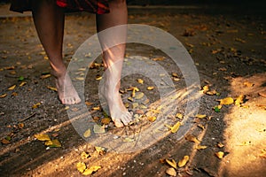 Young woman walking barefoot through autumn leaves