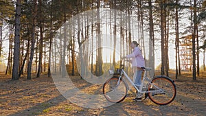 Young woman walking with bicycle in autumn coniferous forest - slow motion