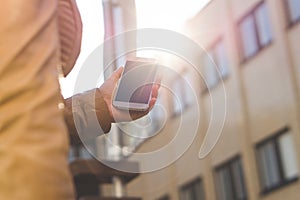 Young woman walking and carrying smartphone in sunshine. Close up of girl holding mobile phone in hand.