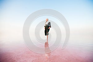 Young woman walking on Dead Sea with beautiful sky at pink sunrise