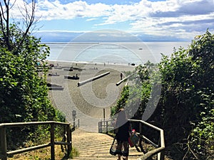 A young woman walking down the stairs facing outwards towards wreck beach in Vancouver, BC.