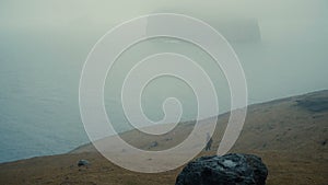 Young woman walking through the field on the shore of the sea and thinking, exploring the nature of Iceland.