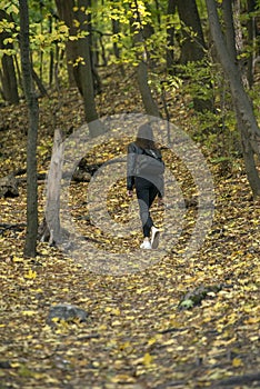 Young woman walking in the forest and enjoys autumn. Girl walks through the wood, fallen leaves under feet. Outdoor walk