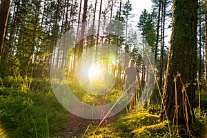 Young woman walking in forest path at sunset.