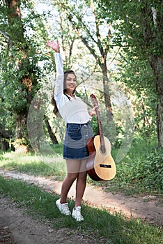 Young woman walking in the forest and playing guitar, summer nature, bright sunlight, shadows and green leaves, romantic feelings