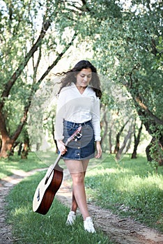 Young woman walking in the forest and playing guitar, summer nature, bright sunlight, shadows and green leaves, romantic feelings