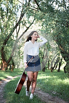 Young woman walking in the forest and playing guitar, summer nature, bright sunlight, shadows and green leaves, romantic feelings