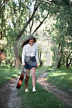 Young woman walking in the forest and playing guitar, summer nature, bright sunlight, shadows and green leaves, romantic feelings