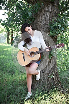 Young woman walking in the forest and playing guitar, summer nature, bright sunlight, shadows and green leaves, romantic feelings