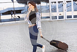 Young woman walking with luggage suitcase and talking smartphone, vacations, travel and active lifestyle concept