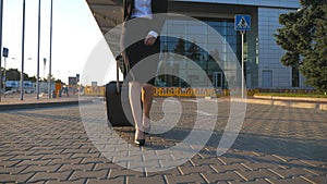 Young woman walking near airport parking with her luggage at sunset time. Female legs in high heels stepping at sidewalk