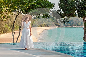 Young woman walking near swimming pool with sea view in modern tropical resort