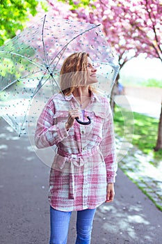 Young woman walking in park with transparent umbrella during sakura