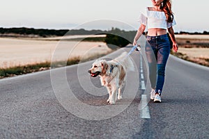 young woman walking by the road with her golden retriever dog at sunset. Pets outdoors