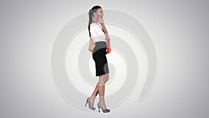 Young woman walking with shopping bags talking on mobile phone on gradient background.