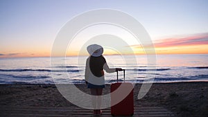 Young woman walking with a suitcase on the beach