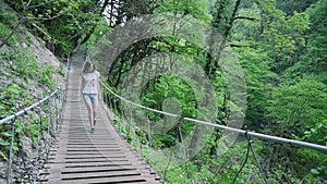 Young woman is walking on a suspension bridge in a forest in the mountains