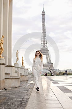 Young woman walking on Trocadero square near gilded statues and Eiffel Tower.