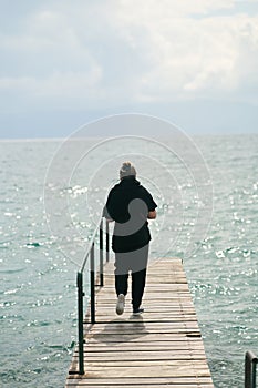 A young woman walking walking along the pier on Lake Ohrid in Macedonia. View from the back