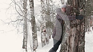 A young woman walking in winter forest and hugging a tree