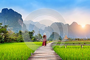 Young woman walking on wooden path with green rice field in Vang Vieng, Laos photo