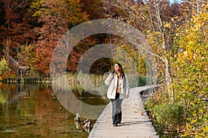 Young woman walking on a wooden pier and admiring the beautiful yellow autumn forest